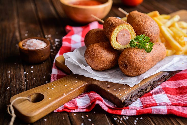 A pile of corn dogs on a cutting board.