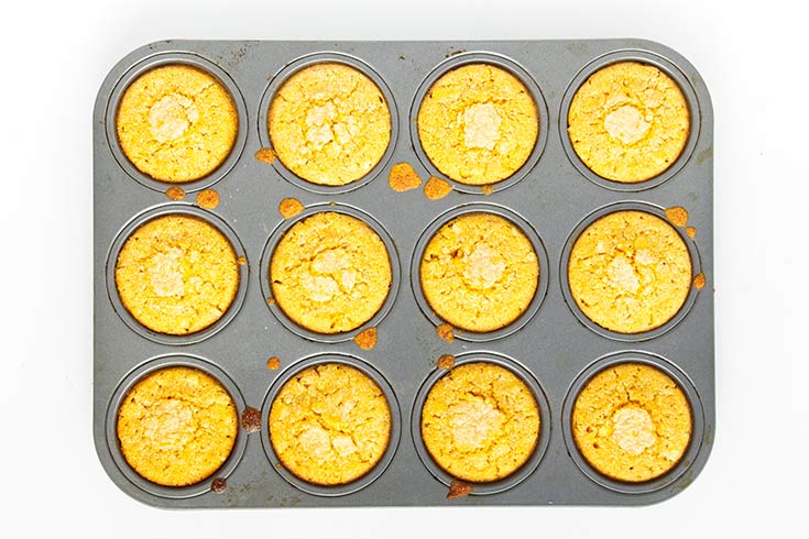 Baked cornbread muffins cooling in the muffin pan they were baked in.
