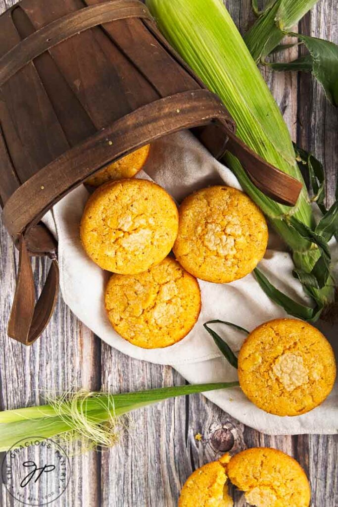 A basket on its side with cornbread muffins coming out of it onto a wood table.