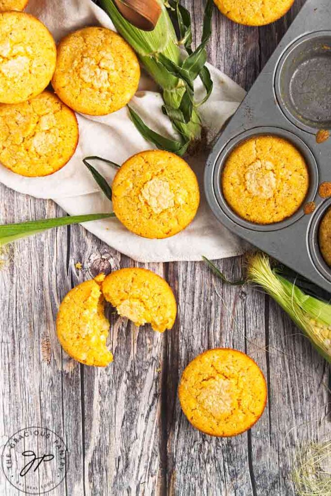 An overhead view of cornbread muffins sitting on a table next to the pan they were baked in.