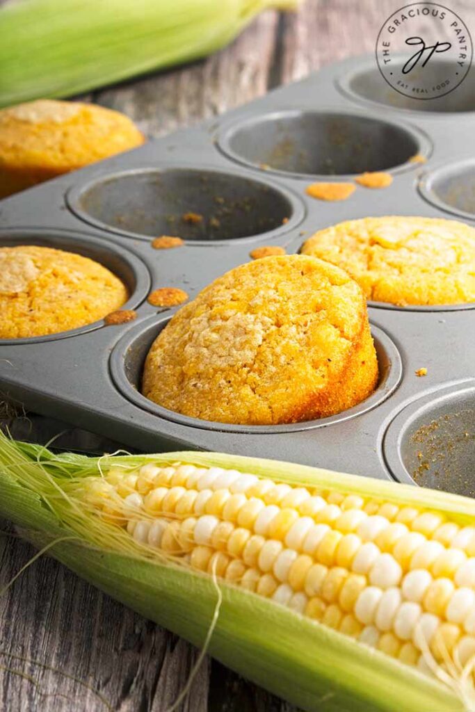 A closeup of a cornbread muffin popped up partially out of the muffin tin.