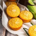 Several cornbread muffins laying on a towel on a wood table.