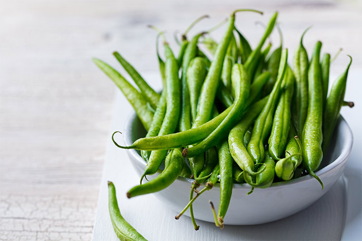 A white bowl filled with fresh green beans.