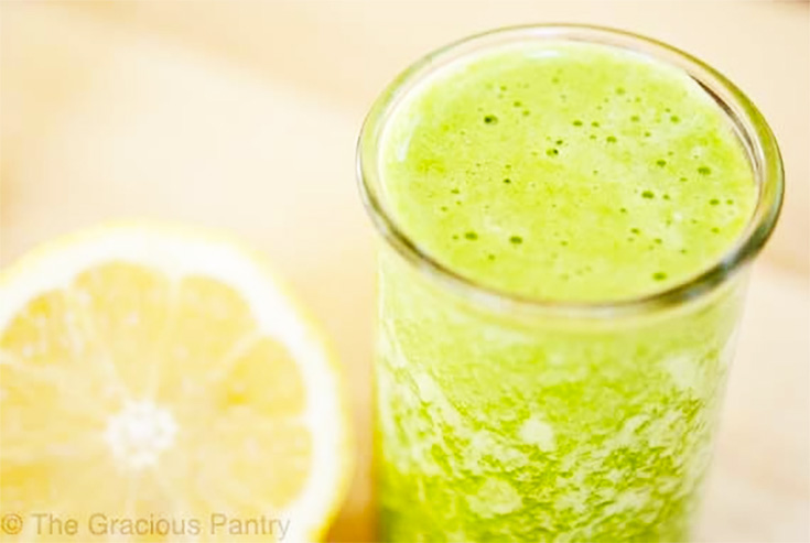 A small glass of green lemon pineapple smoothie sits next to a half of a lemon.
