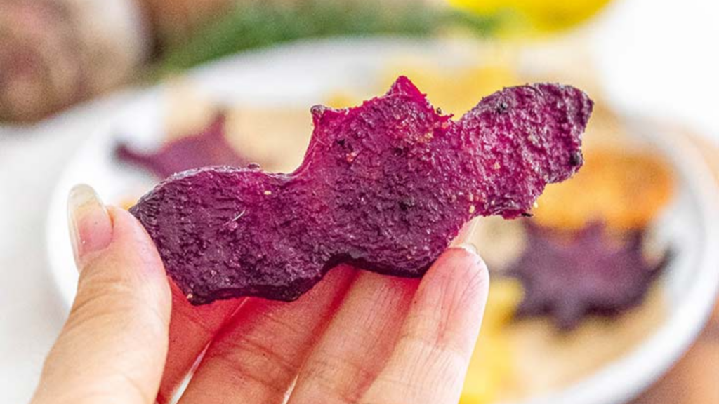 A hand holds a purple halloween bat cut from a beet slice.