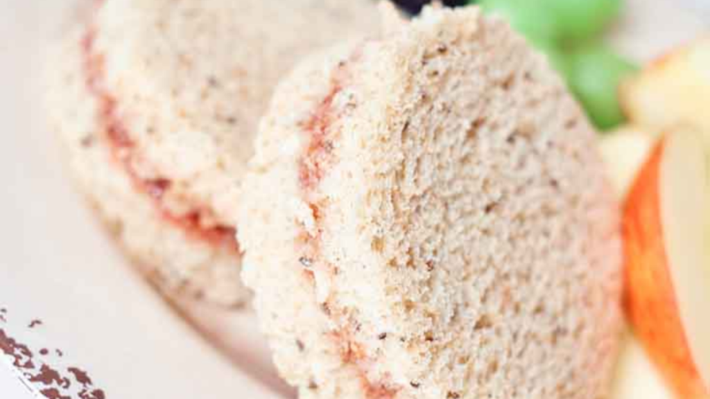 A closeup of jam sandwiches next to some sliced apples.