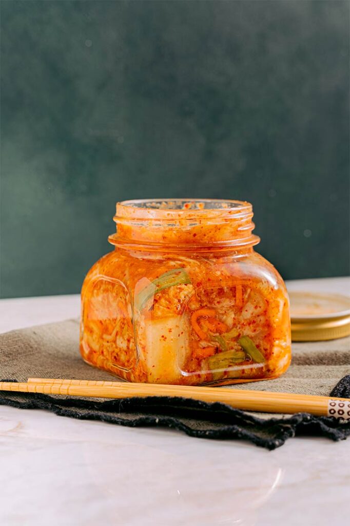 A side view of a clear jar filled with kimchi.