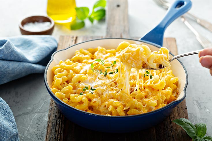 A spoon lifts some macaroni and cheese out of a blue skillet.