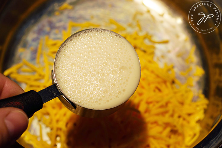 Adding milk to grated cheese in a pot.