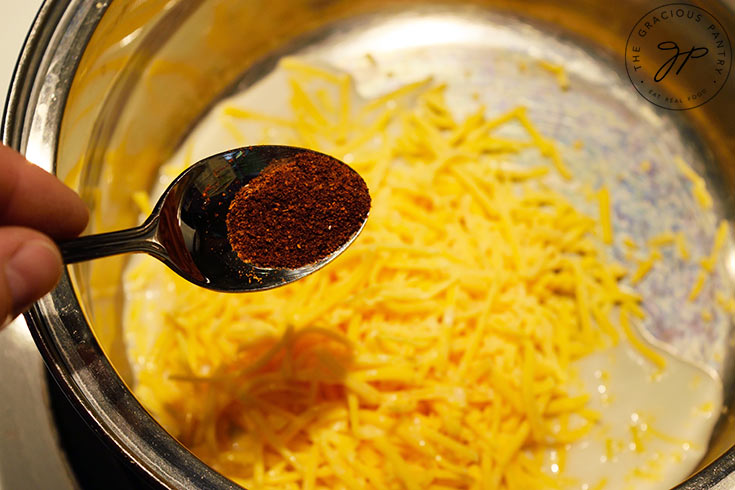 Adding seasoning to cheese and milk in a pot.