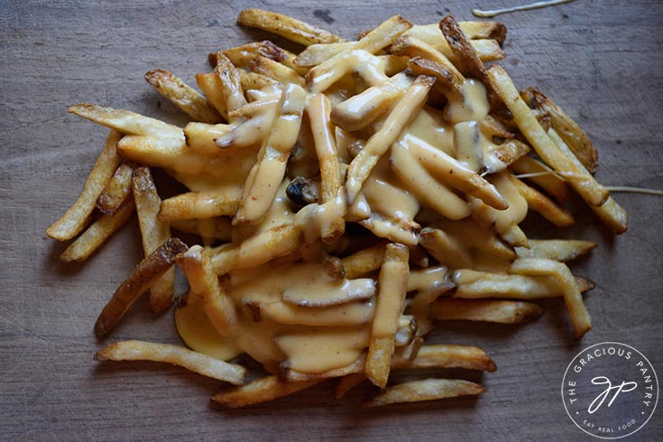 French fries piled on a wood cutting board and topped with nacho cheese sauce.