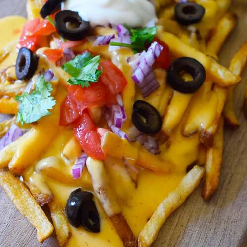 Nacho fries topped with cheese sauce and fresh, chopped veggies with a dollop of sour cream