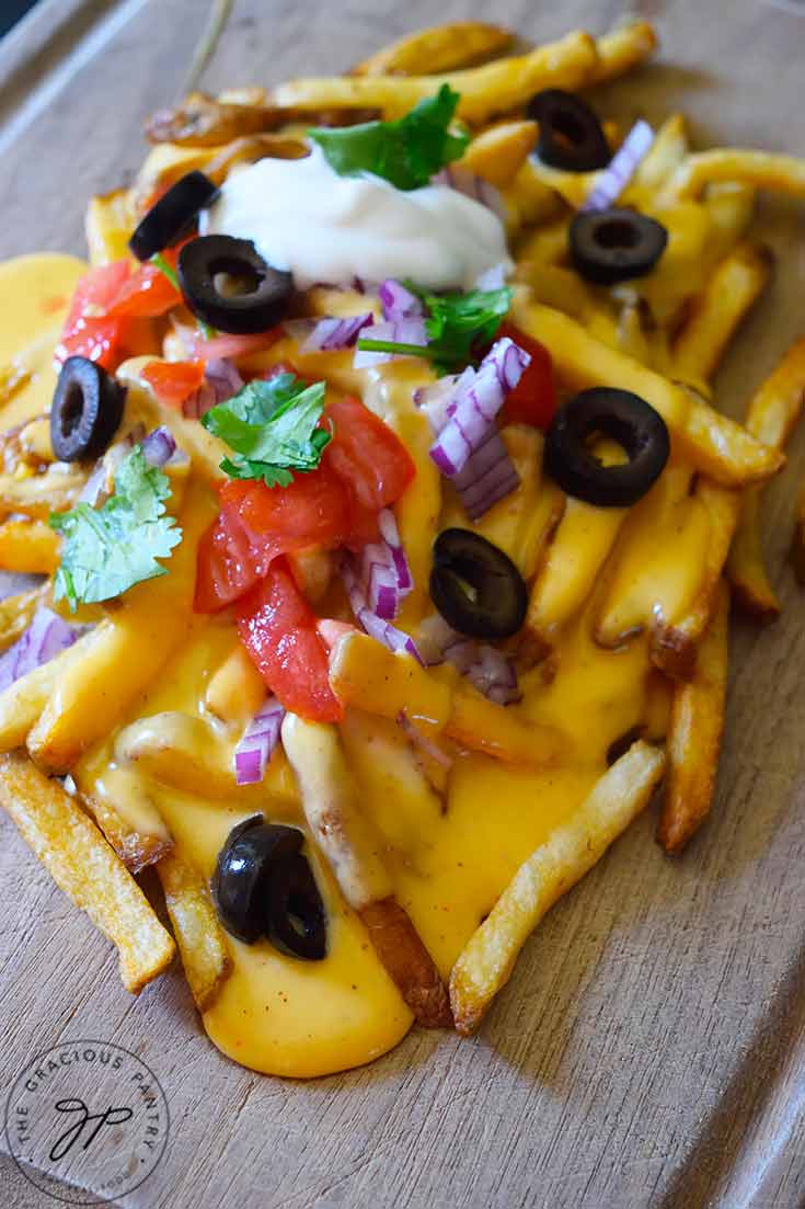 Nacho fries topped with cheese sauce and fresh, chopped veggies with a dollop of sour cream