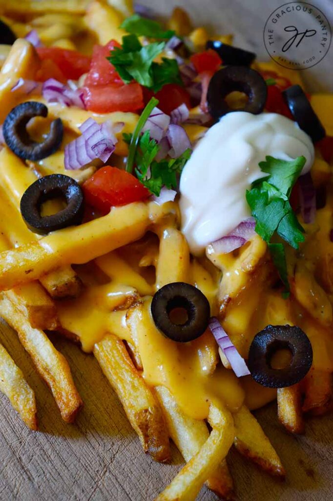 A closeup of a pile of nacho fries on a wood cutting board.