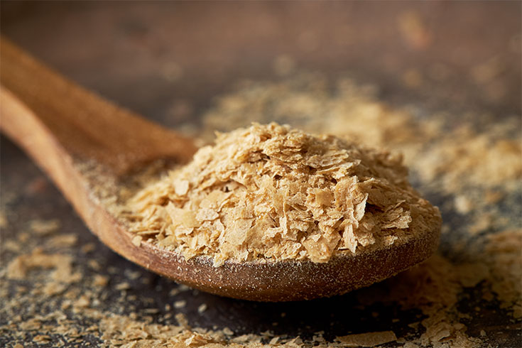 Closeup of nutritional brewers yeast flakes in wooden spoon.
