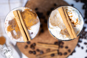 An overhead view of two glasses filled with pumpkin spice latte and topped with cinnamon sticks.