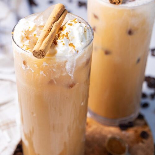 A side view of two glasses filled with pumpkin spice latte.