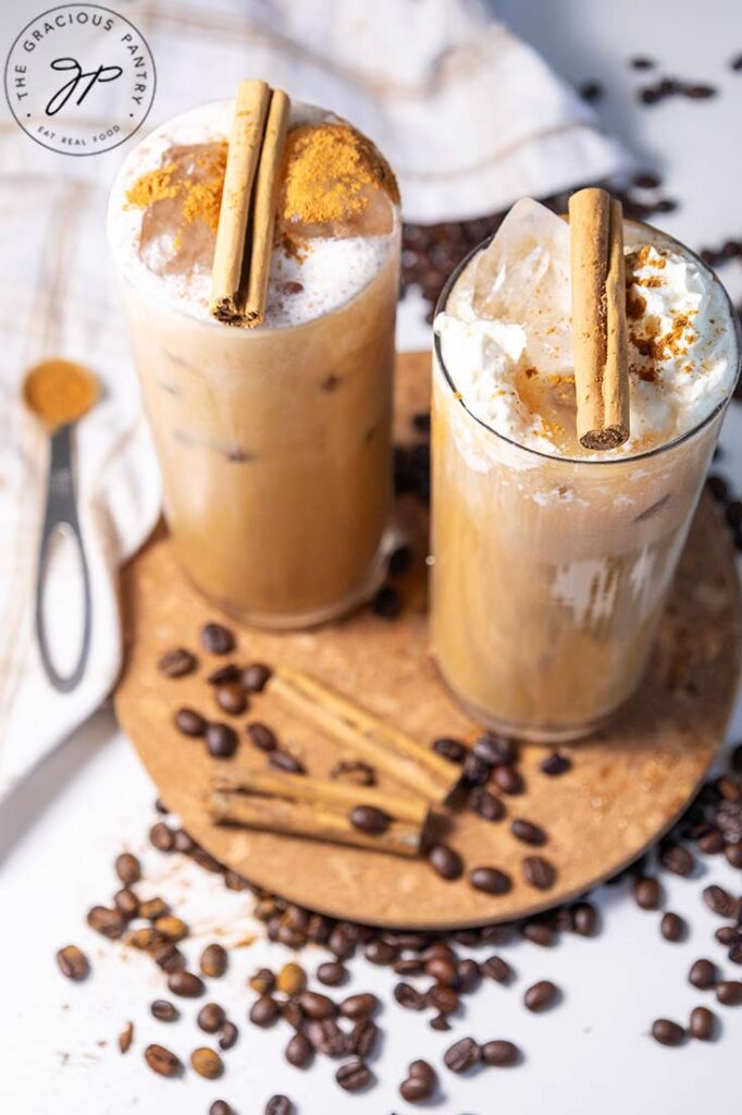 A slightly overhead view of two glasses, side by side, filled with pumpkin spice latte and garnished with cinnamon sticks.