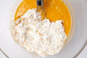 Adding dry ingredients to the wet ingredients in a large mixing bowl.