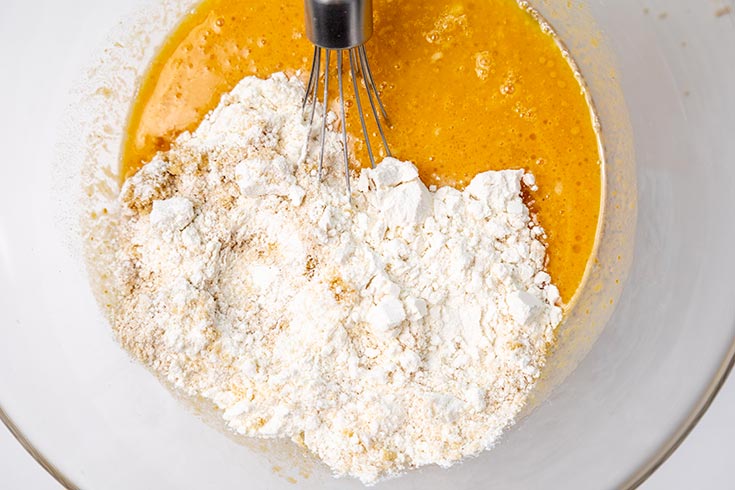 Adding dry ingredients to the wet ingredients in a large mixing bowl.