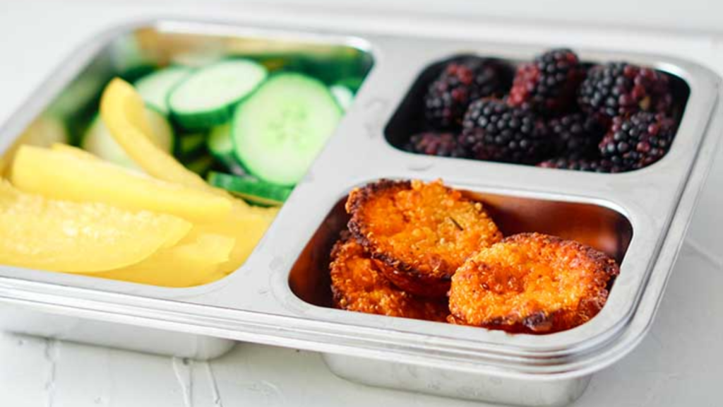 A bento tray with fruits, veggies and some quinoa muffins.