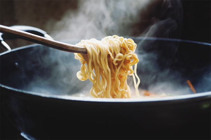 A tong lifts ramen noodles out of a black pot.