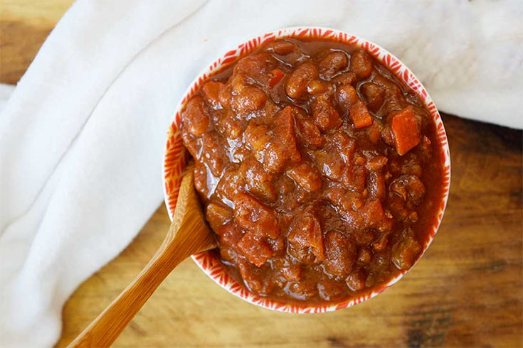 An overhead view of a bowl filled with ranch style beans. A wooden spoon rests in the bowl and beans.
