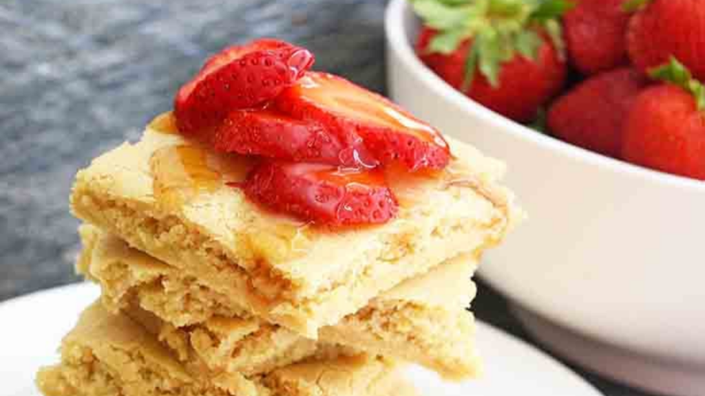 A stack of square cut sheet pan pancakes with fresh strawberry slices on top.