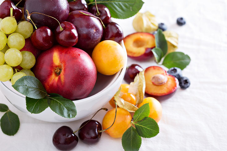 A white bowl filled with grapes and stone fruits. Plums, cherries, a nectarine and an apricot.