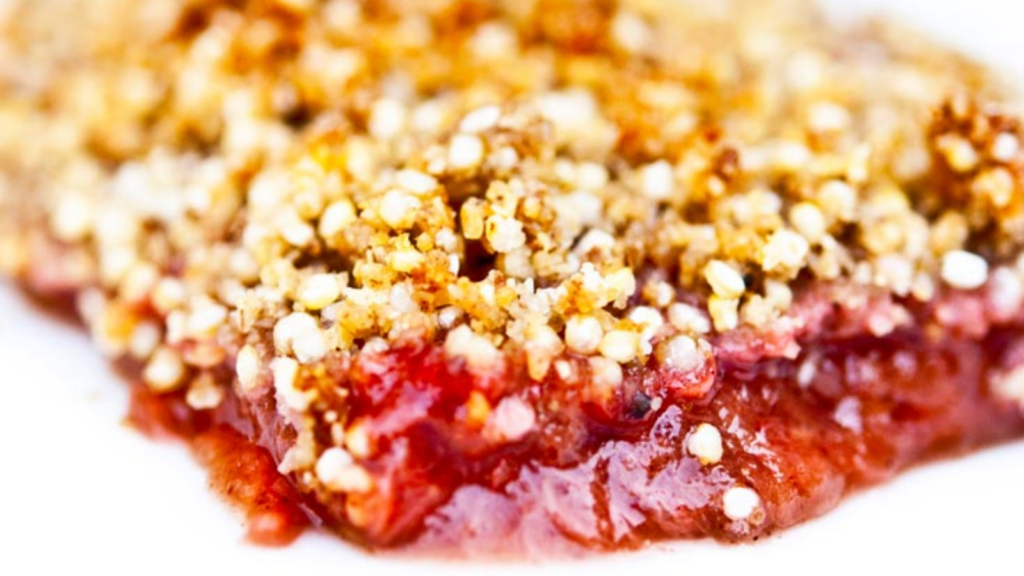 A closeup of a slice of strawberry rhubarb crisp on a white plate.