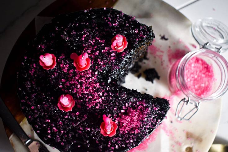 An overhead view of a chocolate cake with pink sugar and candles on top of black frosting.