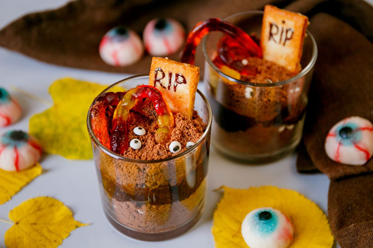 Two glass cups with chocolate jello, cookie crumbs, candy eyes and worms on top.