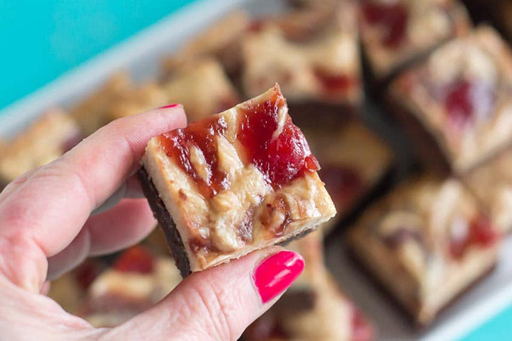 A hand holds up a peanut butter and jelly cream cheese brownie.