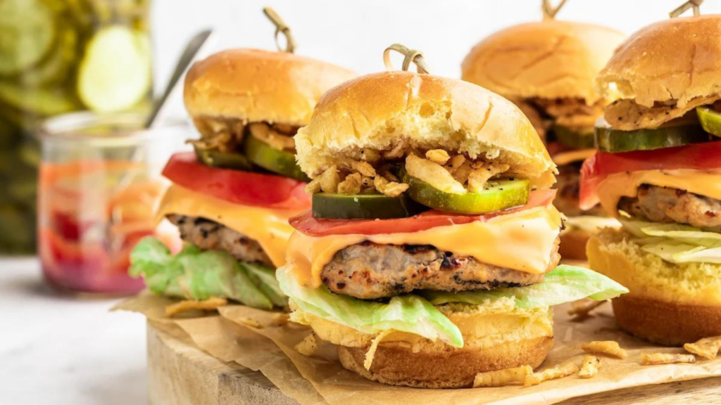 Four turkey burger sliders sitting on a wood cutting board.