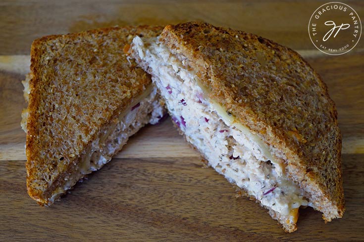 An air fryer tuna melt cut in half and laying on a wooden surface.