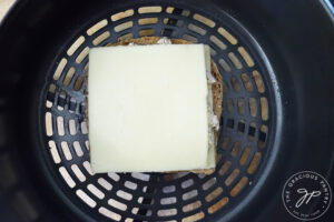 A top layer of cheese added to a tuna melt in an air fryer basket.