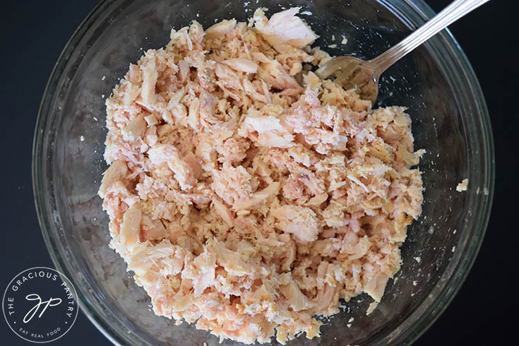 Tuna in a glass mixing bowl, broken apart by a fork which rests in the bowl.