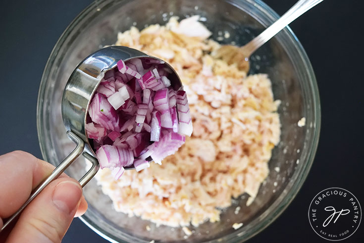 Adding chopped red onions to tuna in a mixing bowl.