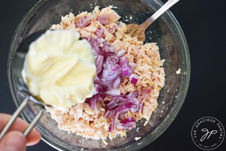Adding mayo to a bowl of tuna and red onions in a mixing bowl.