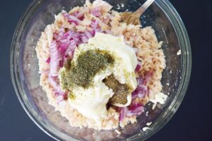 Pepper added to tuna salad ingredients in a glass mixing bowl.