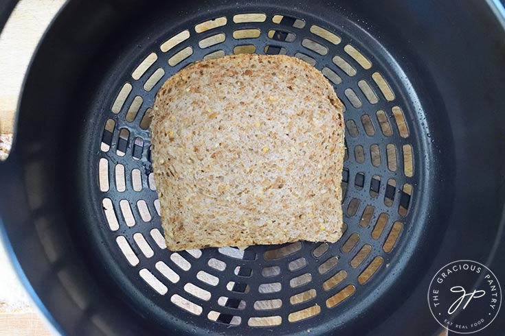A slice of bread laying in an air fryer basket.