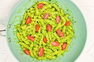 Halved grape tomatoes added to pasta and avocado sauce in a skillet.