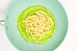 Cooked rotini pasta added to Avocado Pasta sauce in a skillet.