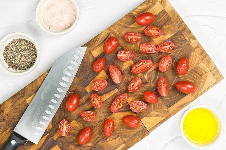 Grape tomatoes cut in half, laying on a cutting board.