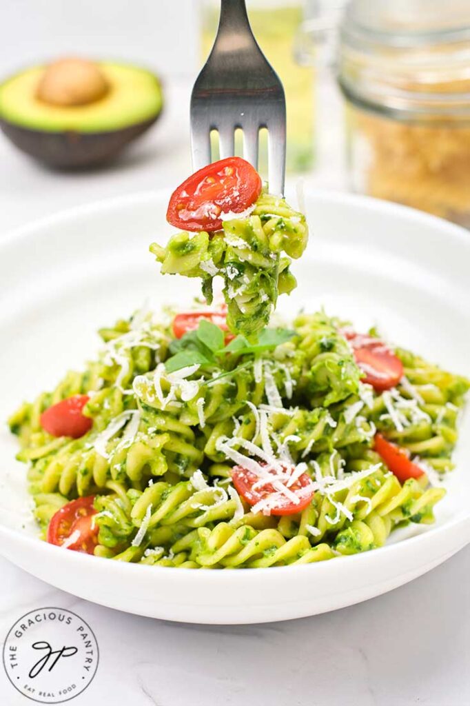 A fork holds a forkful of Avocado Pasta over a white bowl filled with it.