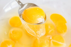 A spoon lifts an egg yolk out of a bowl.