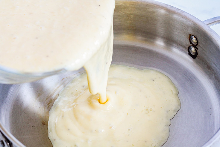 Pouring an egg mixture into a frying pan to make scrambled eggs.