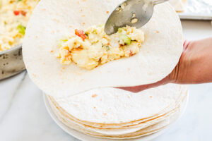 Placing a spoonful of Healthy Breakfast Taquitos filling into a tortilla.