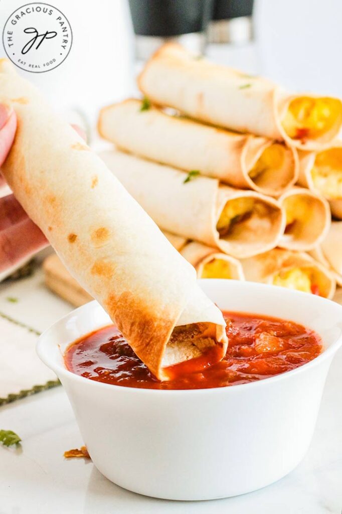 A single Healthy Breakfast Taquito being dipped into some red sauce.