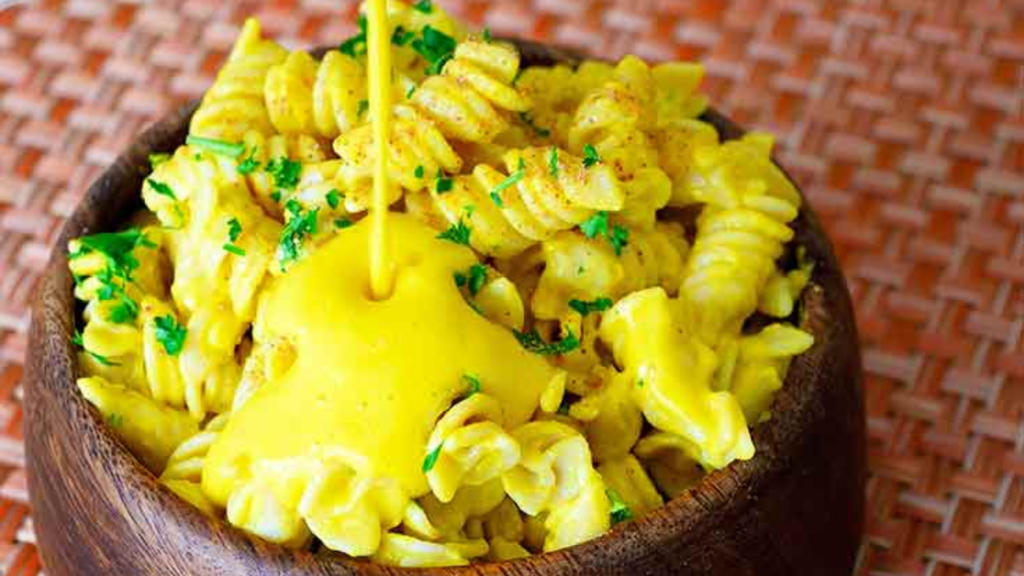 Butternut Squash Pasta Sauce being poured over pasta in a wooden bowl.